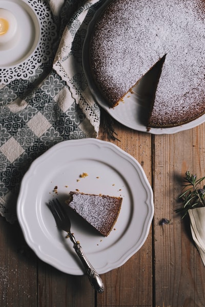 棕色桌子上的圆形白色陶瓷盘子，上面放着切好的蛋糕和叉子